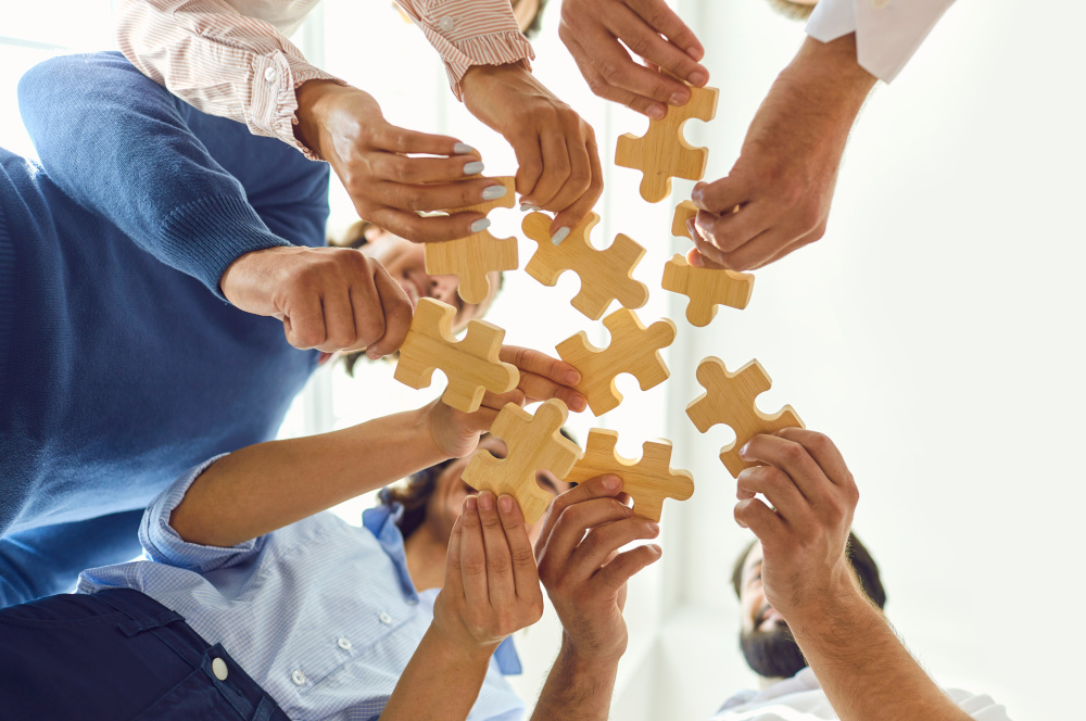 Mehrere Hände halten Holzpuzzle-Stücke in die Mitte.